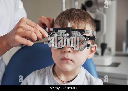 Petit garçon avec phoropter dont il les yeux dans le cabinet du médecin Banque D'Images