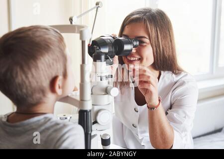 Le dispositif de réglage. Petit garçon ayant pour tester ses yeux avec un appareil optique spécial par femme médecin Banque D'Images