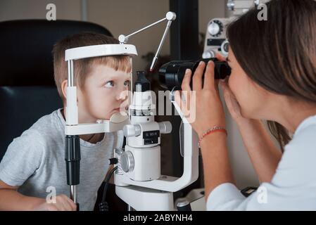 Petit garçon ayant pour tester ses yeux avec un appareil optique spécial par femme médecin Banque D'Images