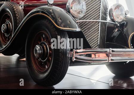 Fermer à l'avant et vue latérale d'une voiture rétro rouge chrome avec Spotlight, bouclier avant et le radiateur, roues étroites avec une arche au-dessus, un pneu de secours et en bois Banque D'Images