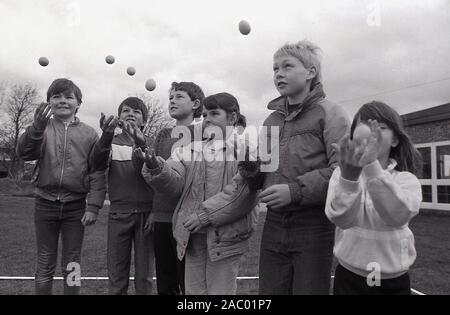 Années 1980, historique, enfants pratiquant le lancement et la capture d'un oeuf i préparation pour la compétition traditionnelle de lancement d'oeufs, Angleterre, Royaume-Uni. Le jet d'oeufs est une activité de deux personnes qui exige le lobbying à distance et la capacité de prendre. Chaque membre de l'équipe commence par se tenir debout à dix mètres de distance, s'étalant après chaque prise réussie. Mais... lâchez ou cassez l'œuf et vous êtes sorti ! On pense que le lancement d'oeufs a eu lieu pour la première fois dans les années 1300, devenant progressivement un sport informel appelé le 'jeu d'oeufs', joué dans les foires de pays et les fètes. Banque D'Images