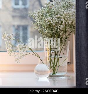 Gypsophila bouquet sur la fenêtre dans un vase de verre au crépuscule. Banque D'Images