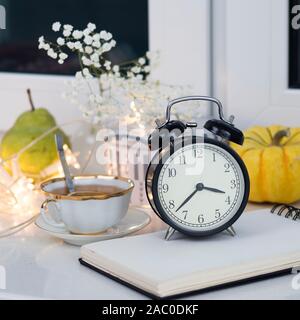 Gypsophila bouquet sur la fenêtre dans un vase de verre au crépuscule. Tasse de thé au citron. L'horloge indique trois heures et demi. Banque D'Images