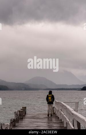 Vue arrière d'une femme portant un sac à dos contre lac Nahuel Huapi à Brava Bay pier sur un jour nuageux dans le Parc National Los Arrayanes, Patagonie Banque D'Images