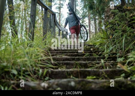 Homme fort est titulaire d'une bicyclette sur son épaule et monte les marches recouvert d'herbe. Banque D'Images