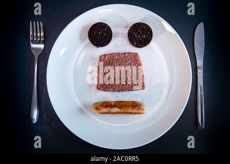 Saucisse carrée et sanglier noir disposés en forme de visage souriant sur une assiette, marquant de nouveaux contrats d'approvisionnement Asda pour We Hae Meat et Simon Howie, Écosse, Royaume-Uni Banque D'Images