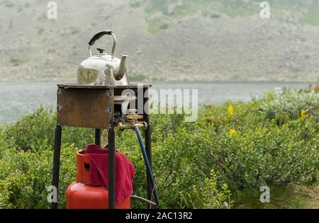 Le tourisme, les vieux peuplements classique théière et soleil sur un brûleur à gaz en métal rouillé sur l'arrière-plan d'une grande montagne Banque D'Images