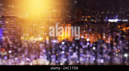 Ville sous la pluie dans la nuit. La fenêtre en verre avec des gouttes de flou. L'éclairage des rues et l'éblouissement réfléchi dans l'eau de pluie à l'avant-plan Banque D'Images