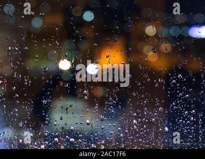 La pluie à l'extérieur. Gouttes d'eau sur une vitre dans la nuit. Le mauvais temps dans la ville. La lumière des lanternes dans un beau bokeh. Banque D'Images