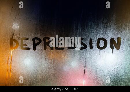 Le mot dépression écrit par doigt sur le verre humide de nuit avec lumières floues en arrière-plan. Banque D'Images