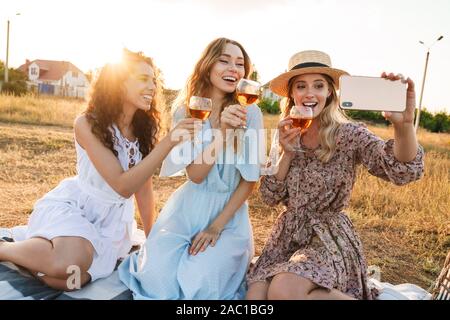 Photo de rire belle femmes prenant des photos sur téléphone cellulaire tout en selfies drinking red wine à jour ensoleillé durant la campagne Banque D'Images