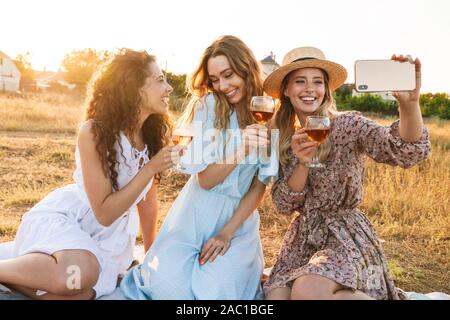 Photo de nice smiling women taking photo selfies sur téléphone cellulaire tout en buvant du vin rouge à la campagne au cours de journée ensoleillée Banque D'Images