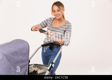 Image of nice woman taking photo son bébé dans la poussette en marchant isolated over white background Banque D'Images