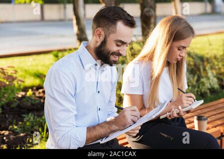 Photo d'un jeune homme heureux et concentré d'affaires femme en extérieur dans la nature park à écrire des notes dans des carnets. Banque D'Images