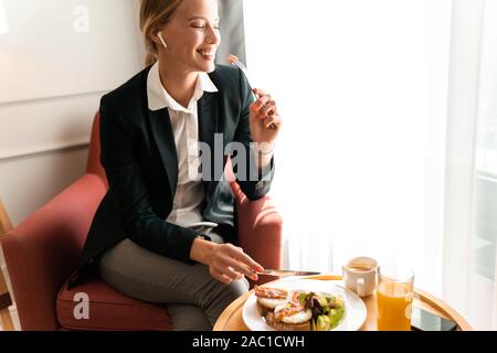 Photo d'un jeune gai beautiful happy blonde optimiste positive business woman s'asseoir à l'intérieur des maisons ont un dîner. Banque D'Images