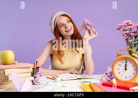 Photo de l'élève excité girl holding paper plane alors que faire des devoirs à 24 isolated over fond violet Banque D'Images