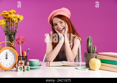 Image de charmant teenage girl smiling tout en étudiant avec les livres d'exercice à 24 sur fond violet isolés Banque D'Images