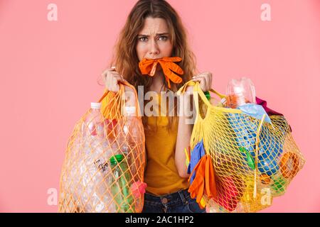 Photo de femme peur confus avec gant en caoutchouc dans son espèce de sacs de déchets plastiques avec la tenue plus isolé sur fond rose Banque D'Images