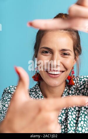 Portrait d'une charmante jeune femme portant chemise et des boucles d'isolés sur fond bleu, looking at camera, feignant de t Banque D'Images