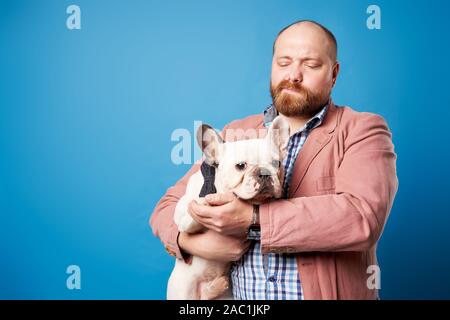 Homme avec bouledogue français dans ses bras sur fond bleu vide en studio Banque D'Images