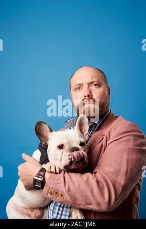 Homme chauve avec bouledogue français d'armes sur fond bleu vide en studio Banque D'Images