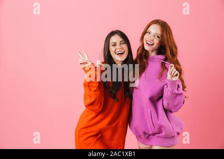 Deux filles gaies isolés sur fond rose, hugging Banque D'Images