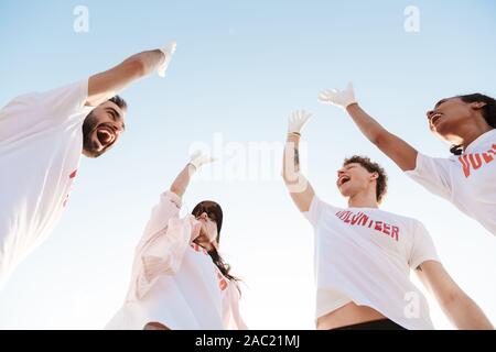 Groupe de jeunes joyeux amis volontaires de déchets, nettoyage de plage, offrant un rapport cinq Banque D'Images
