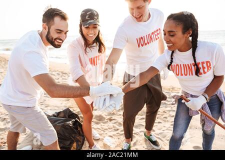 Groupe de jeunes joyeux amis volontaires de déchets, nettoyage de plage, offrant un rapport cinq Banque D'Images