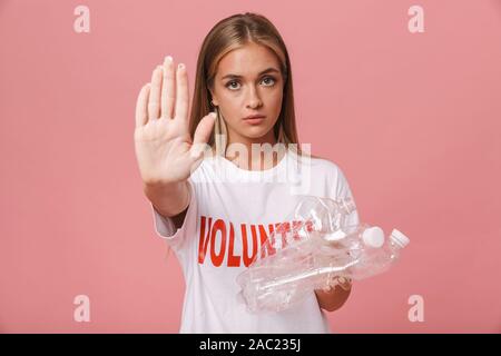 Certain jeune volontaire girl isolés sur fond rose, montrant le geste d'arrêt tout en maintenant les bouteilles en plastique Banque D'Images