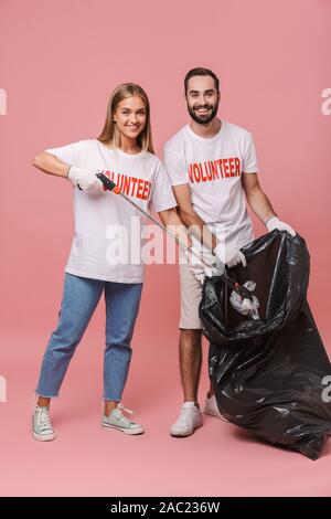 Toute la longueur d'un jeune couple bénévoles isolés sur fond rose, mettre les ordures dans un sac Banque D'Images