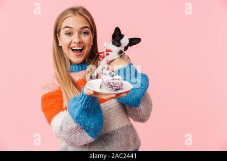 Belle jeune fille heureux montrant morceau de gâteau tout en tenant un chihuahua plus isolé sur fond rose Banque D'Images