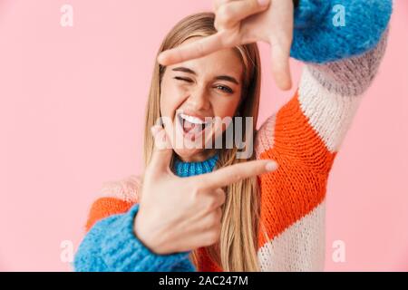 Portrait d'une belle jeune fille belle excité portant sweater isolés sur fond rose, faisant semblant de prendre une photo avec les mains Banque D'Images