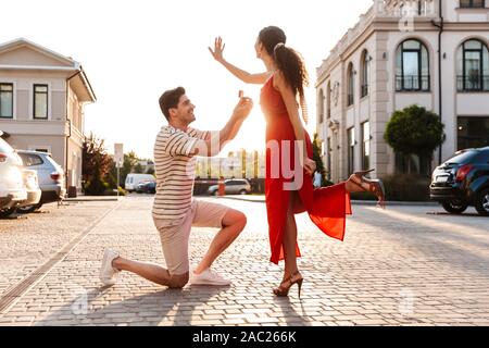 Image of handsome man making proposition de mariage à sa petite amie avec anneau en boite cadeau en marchant au city street Banque D'Images