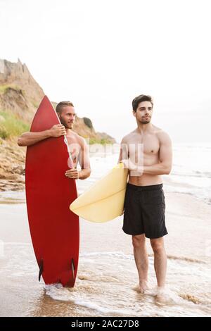 Image d'un jeune homme gai deux positifs d'amis surfeurs avec surfings sur une plage à l'extérieur. Banque D'Images