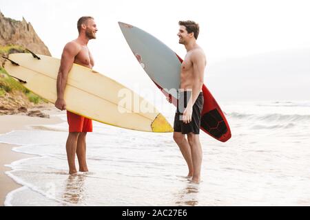 Image d'un jeune homme gai deux positifs d'amis surfeurs avec surfings sur une plage à l'extérieur. Banque D'Images