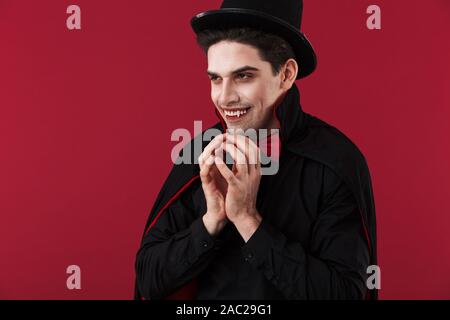 Image de l'homme vampire mystique avec le sang et de crocs en noir costume halloween isolated over red wall Banque D'Images