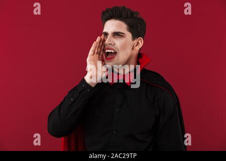 Image de l'homme vampire avec crochets en noir costume halloween crier isolated over red wall Banque D'Images