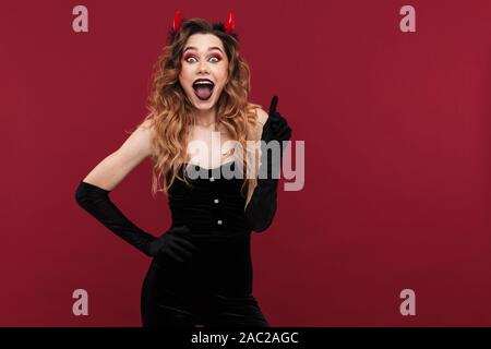 Image femme rusé surpris démon en costume de carnaval sur fond rouge isolé mur montrant silence geste. Banque D'Images