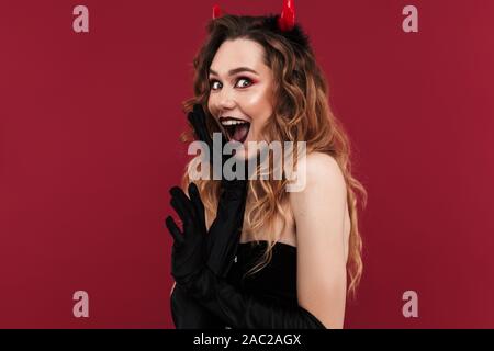 Image of surprised woman démon en costume de carnaval sur fond Mur isolé rouge. Banque D'Images