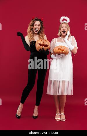 Image femme joyeuse et positive en ange démon curiepe isolated over red wall background holding pumpkin. Banque D'Images