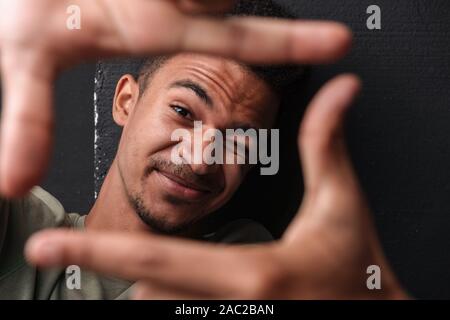 Image de l'african american guy looking at camera tout en tenant tête à photos selfies sur fond noir isolé Banque D'Images
