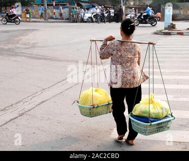 Vietnamienne avec le traditionnel panier crossing les rues de Hanoi, la capitale du Vietnam. Banque D'Images