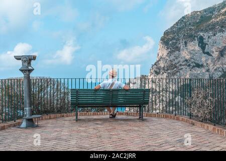 Man wearing hat s'asseoir sur un banc le regard sur la mer Tyrrhénienne en jardin d'Auguste en Capri Banque D'Images