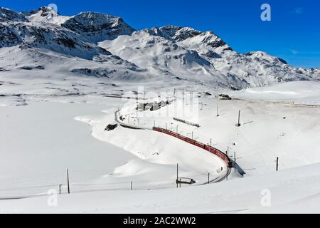 Route des chemin de fer rhétique avec le Bernina Express dans le paysage alpin d'hiver au col de la Bernina, Engadine, Grisons, Suisse Banque D'Images