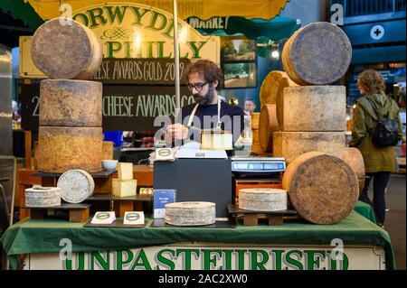 Londres - le 27 septembre 2019 : l'utilisation d'un smartphone commerçant lors de l'attente de clients à un décrochage du marché du fromage à Borough Market, London. Banque D'Images