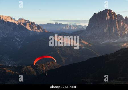 Parapentiste avec parachute rouge vole au dessus des montagnes remplies d'arbres dans la lumière du soleil Banque D'Images