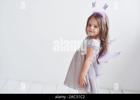 Côté photo. Jolie petite fille dans le costume fée debout dans la pièce avec un fond blanc Banque D'Images