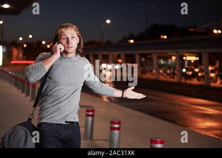 Jeune homme stylih alking par la nuit Street près de la route et avoir une conversation au téléphone Banque D'Images