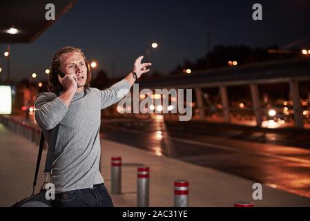 Les gestes de la main active. Jeune homme élégant marche à travers la nuit, à proximité de la route et avoir une conversation au téléphone Banque D'Images