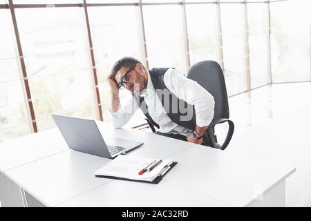 Employé de bureau fatigué assis dans la salle et à la recherche à spacey son ordinateur portable Banque D'Images